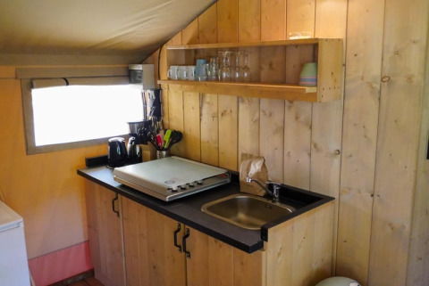 Kitchen area in a safari tent at Camping Pittoresque, France, with sink, shelf, and utensils shown.