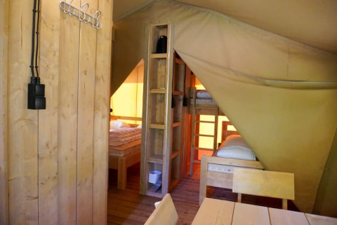 Interior de una tienda safari con baño privado en Camping Pittoresque, camas de madera y mesa en Francia.
