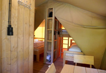 Interior de una tienda safari con baño privado en Camping Pittoresque, camas de madera y mesa en Francia.