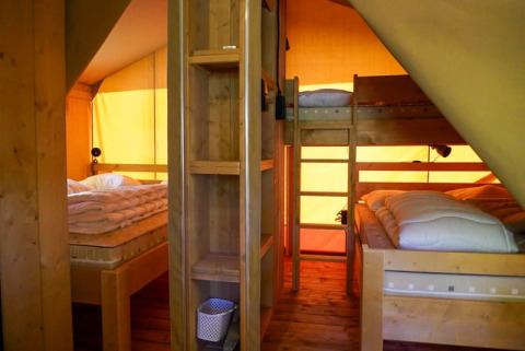 Interior de una tienda safari con literas y cama doble en Camping Pittoresque, Francia, con luz cálida.