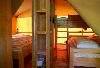 Interieur van een safaritent met stapelbed en tweepersoonsbed bij Camping Pittoresque in Frankrijk.