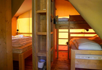 Interior de una tienda safari con literas y cama doble en Camping Pittoresque, Francia, con luz cálida.