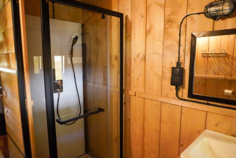 Baño con cabina de ducha y paredes de madera en una tienda safari con baño privado en Camping Pittoresque, Francia.