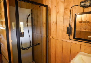 Badkamer met een douchecabine en houten muren in een safaritent met privé sanitair op Camping Pittoresque, Frankrijk.
