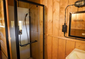 Baño con cabina de ducha y paredes de madera en una tienda safari con baño privado en Camping Pittoresque, Francia.