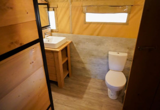 Badeværelse i et safaritelt med moderne toilet og håndvask på Camping Pittoresque i Frankrig.