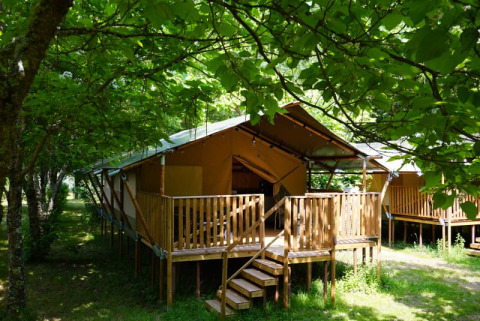 Safari-Zelt mit Sanitäranlagen auf Camping Pittoresque in Frankreich, umgeben von grünen Bäumen.