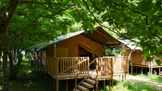 Safaritent met privé sanitair op Camping Pittoresque in Frankrijk, omgeven door groene bomen.