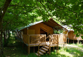 Safari-Zelt mit Sanitäranlagen auf Camping Pittoresque in Frankreich, umgeben von grünen Bäumen.