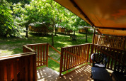 Terraza de madera de tienda safari con baño privado en Camping Pittoresque, rodeada de árboles en Francia.