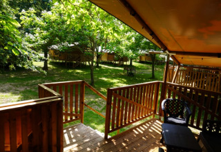 Terrasse en bois d'une tente safari avec sanitaire au Camping Pittoresque, entourée d'arbres en France.