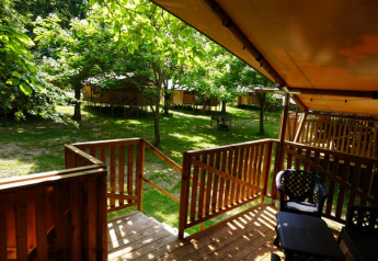 Terraza de madera de tienda safari con baño privado en Camping Pittoresque, rodeada de árboles en Francia.