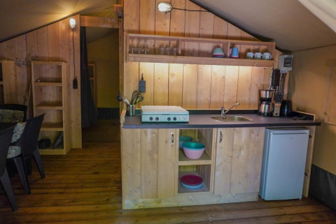 Gemütliche Küchenzeile im Safarizelt mit Holzmöbeln, Kochplatte, Spüle und Minikühlschrank in Frankreich.
