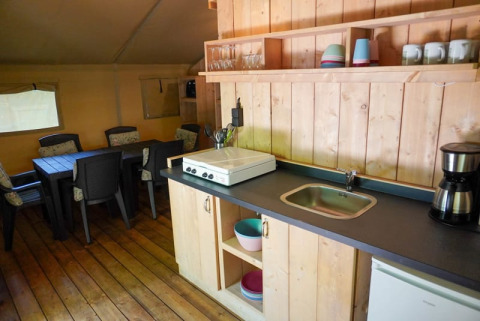 Kitchen and dining area inside a safari tent with sanitary facilities at Camping Pittoresque in France.