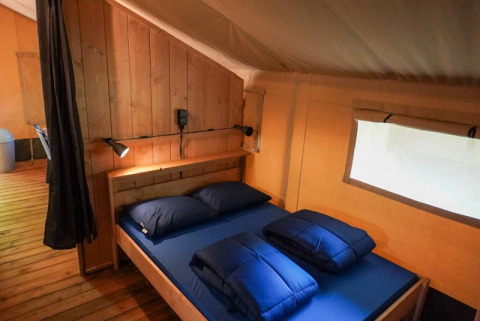 Innenansicht eines Safari-Zeltes mit Holzwänden und Doppelbett auf Camping Pittoresque in Frankreich.