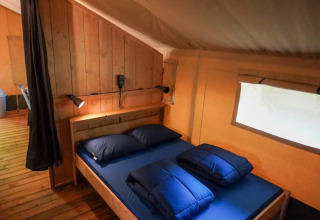 Inde i et safari telt med trævægge, dobbeltseng og vindue på Camping Pittoresque i Frankrig.