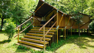 Photo of a safari tent named Duo Lodge, elevated on wooden stilts, surrounded by lush green trees and grass.
