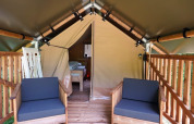 Vista interior de la tienda safari Duo Lodge con asientos de madera en la terraza en Camping Pittoresque, Francia.