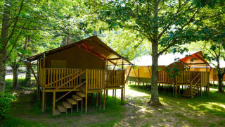 Tente safari avec toilettes sur terrasse en bois, entourée d’arbres dans un cadre verdoyant et naturel.