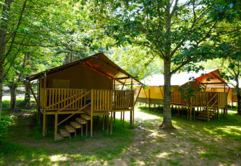 Tienda safari con baño elevada sobre plataforma de madera, entre árboles en un entorno verde y natural.