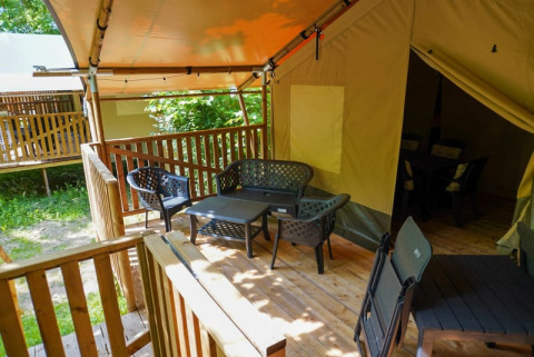Area salotto all'aperto su veranda in legno davanti a tenda safari con bagno al Camping Pittoresque, Francia.