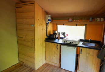 Cucina interna di tenda safari con mobili in legno, fornello, macchina da caffè e frigorifero in Francia.