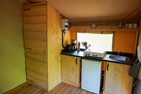Innenküche eines Safari-Zeltes mit Holzschränken, Kochfeld, Kaffeemaschine und Kühlschrank in Frankreich.