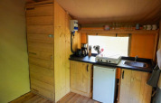 Cucina interna di tenda safari con mobili in legno, fornello, macchina da caffè e frigorifero in Francia.