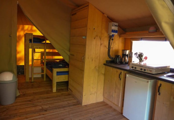 Interior de tienda safari con cocina, nevera, literas y suelo de madera en Camping Pittoresque, Francia.