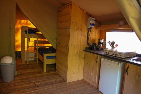 Innenraum eines Safari-Zeltes mit Küche, Kühlschrank, Etagenbetten und Holzfußboden auf Camping Pittoresque, Frankreich.