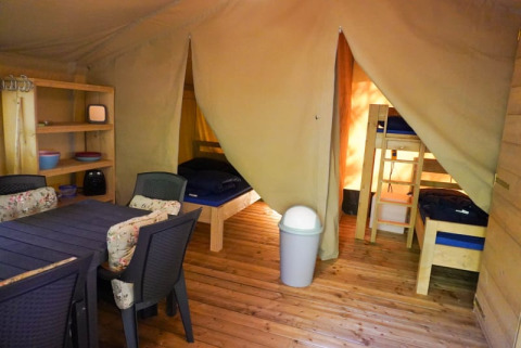 Innenraum eines Safarizelts mit Betten, Esstisch und Regalen auf Camping Pittoresque in Frankreich.