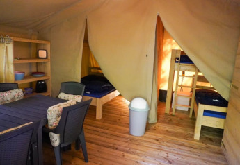 Interior de tienda safari con camas, mesa de comedor y estantes en Camping Pittoresque en Francia.