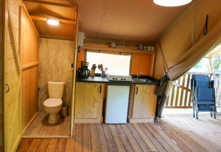 Vista interna di una tenda safari con cucina, bagno e terrazza al Camping Pittoresque in Francia.
