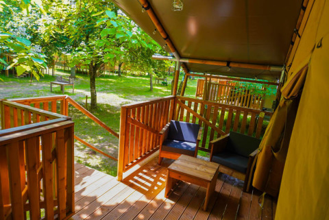 Blick von der Veranda eines Safari-Zeltes auf Camping Pittoresque in Frankreich, von Bäumen umgeben.