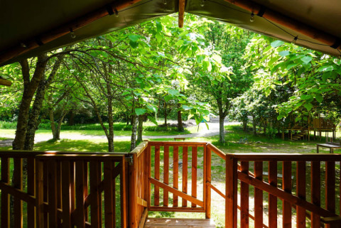 Blick von der Terrasse eines Safarizelts auf Camping Pittoresque in Frankreich auf grüne Bäume und Natur.