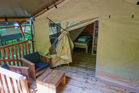 Innen- und Außenansicht eines Safarizeltes auf dem Camping Pittoresque in Frankreich mit Holzmöbeln.
