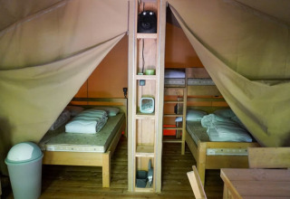 Vista interior de una tienda safari en Camping Pittoresque, Francia, con camas de madera y estanterías.