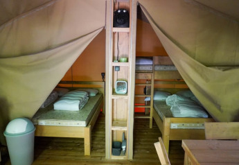 Innenansicht eines Safari-Zeltes auf Camping Pittoresque in Frankreich mit Holzbett und Regalen.