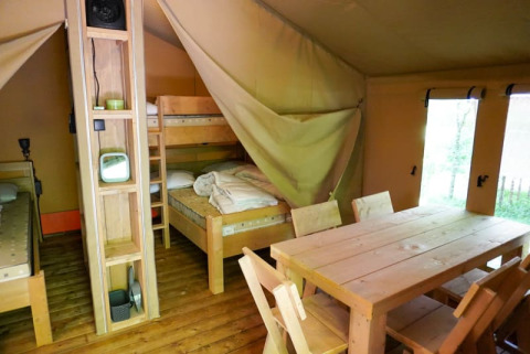 Innenraum eines Safarizeltes auf Camping Pittoresque in Frankreich mit Holzbetten und Esstisch.