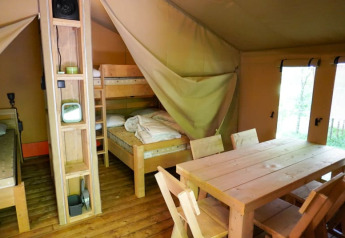 Interior de una tienda safari en Camping Pittoresque, Francia, con literas y mesa de comedor de madera.