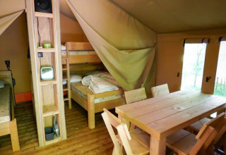 Interior de una tienda safari en Camping Pittoresque, Francia, con literas y mesa de comedor de madera.