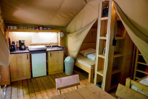 Innenansicht eines Safari-Zelts auf Camping Pittoresque in Frankreich mit Küche und Schlafraum.