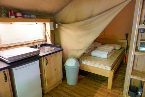 Innenansicht eines Safari-Zeltes mit Bett, Küchenzeile, Spüle und Kühlschrank auf Camping Pittoresque in Frankreich.