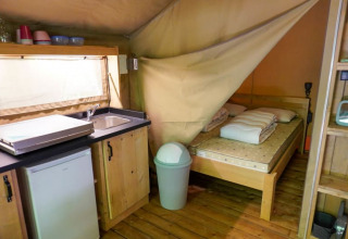 Innenansicht eines Safari-Zeltes mit Bett, Küchenzeile, Spüle und Kühlschrank auf Camping Pittoresque in Frankreich.