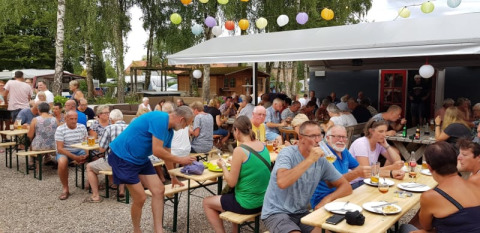 Menschen essen und trinken an langen Tischen unter Lampions beim Safarizelt auf Camping Elbeling in Deutschland.