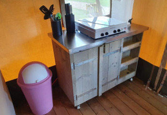 Cocina de tienda safari con cubo rosa, estufa, utensilios y garrafa de agua en Camping Elbeling, Alemania.