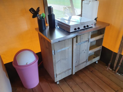 Safari-Zeltküche mit rosafarbenem Mülleimer, Herd, Utensilien und Wasserkanister im Camping Elbeling, Deutschland.