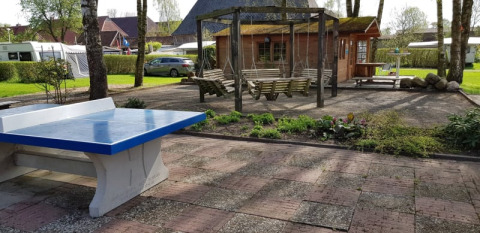 Außenbereich beim Safari tent mit Tischtennisplatte, Schaukeln, Garten und Wohnwagen im Hintergrund.