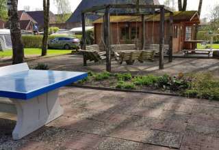 Udendørs område ved Safari tent med bordtennisbord, gyngesæder, have og campingvogne i baggrunden.