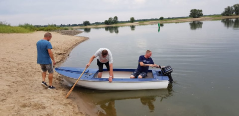 Tre uomini spingono una piccola barca in acqua vicino a una tenda safari e un lago tranquillo.